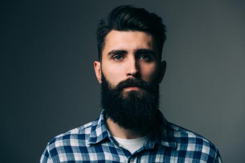 Portrait of masculinity. Portrait of handsome young bearded man looking at camera while standing against grey background