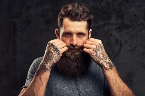 Portrait of a hipster with full beard and stylish haircut, dressed in a gray t-shirt in a studio